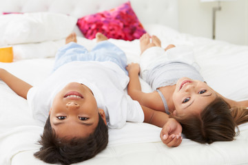 Obraz na płótnie Canvas Children Lying Upside Down On Bed In Pajamas Together