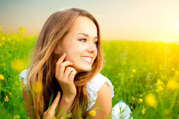 Beauty Girl in the Meadow lying on Green Grass with wild Flowers