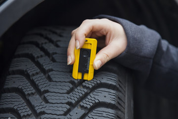 Frau misst Reifenprofil eines Autoreifen
