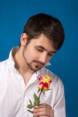 Young man looking to red rose on blue background