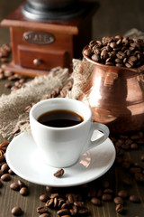 Cup of coffee, pot and grinder on wooden background