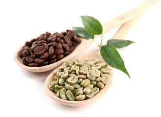 Green  and brown coffee beans in wooden spoons and leaves