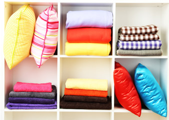 Bright pillows, towels and plaids on shelves, isolated on white