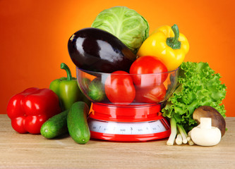 Fresh vegetables in scales on table on orange background