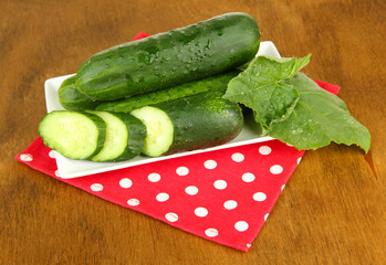 Tasty green cucumbers on color napkin, on wooden background
