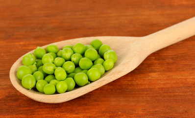 Sweet green peas in spoon on wooden background