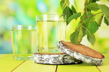 Glasses of birch sap on wooden table, on green background