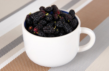 Fototapeta na wymiar Ripe mulberries in cup on table in room