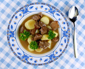 Wild goulash with potato, sauce and spoon on blue plate