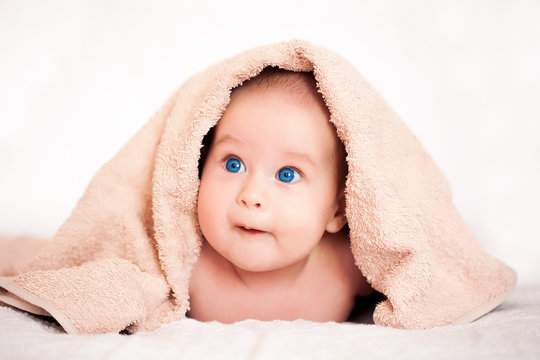 cute baby girl is hiding under the beige terry towel