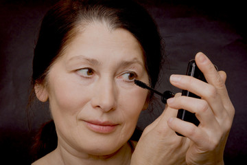 Woman with bare shoulders looks mirror paints eyelashes