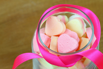 Colorful sugar hearts in glass jar with pink ribbon