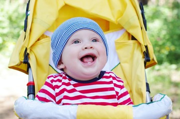 lovely smiling baby boy outdoors on yellow baby carriage