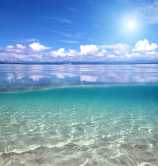 Split view over and under water in the Caribbean sea with clouds reflected on surface and a sandy seabed