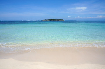 Obraz premium Tropical sandy beach shore with turquoise water and an island at the horizon, Caribbean sea