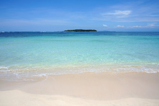 Tropical sandy beach shore with turquoise water and an island at the horizon, Caribbean sea