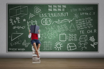 Boy reading book in class sitting on stack of books