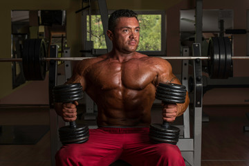 Fototapeta na wymiar shirtless body builder posing with dumbbell at the bench