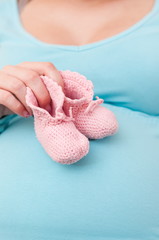 Pregnant Woman (mother) Holding Pink Baby Shoes on her belly.