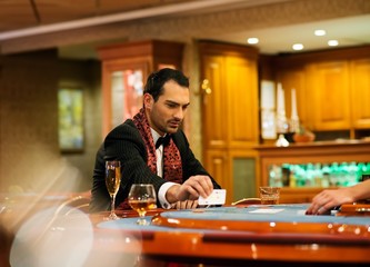 Young handsome man sitting behind poker table with card