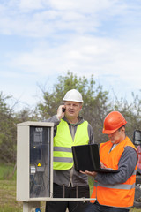 Electricians with PC and folder near switchboard