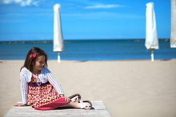 Bambina bella seduta sulla spiaggia