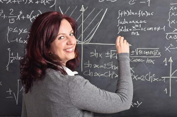 smiling caucasian female teacher with red hair. sociable look. blackboard on the background. teaching and school concept.