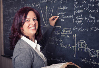 smiling caucasian female teacher with red hair. sociable look. blackboard on the background....