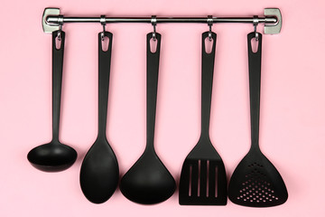 Black kitchen utensils on silver hooks, on pink background