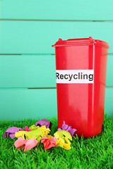 Recycling bin with papers on grass on light blue background