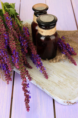 Obraz na płótnie Canvas Medicine bottles and salvia flowers on purple wooden background