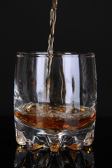Brandy pouring into glass on black background