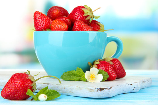Ripe sweet strawberries in cup on blue wooden table