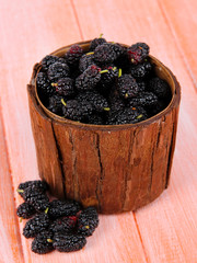 Ripe mulberries in bowl on wooden background