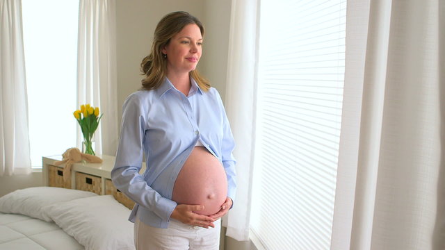 Happy pregnant woman standing by window