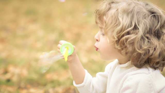 Happy child blowing soap bubbles in autumn park. Slow motion