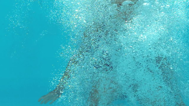 Brunette woman floating underwater in blue swimsuit