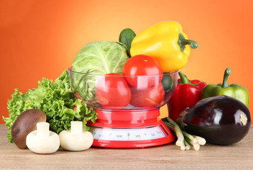 Fresh vegetables in scales on table on orange background