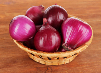 Purple onion in wicker basket on wooden background