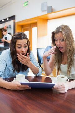 Women looking surprised while holding a tablet