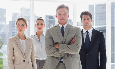 Boss with his arms folded standing with serious colleagues behin