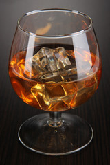 Brandy glass with ice on wooden background