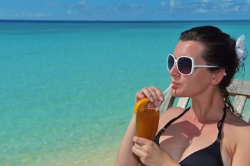 Beautiful young woman with a drink by the sea