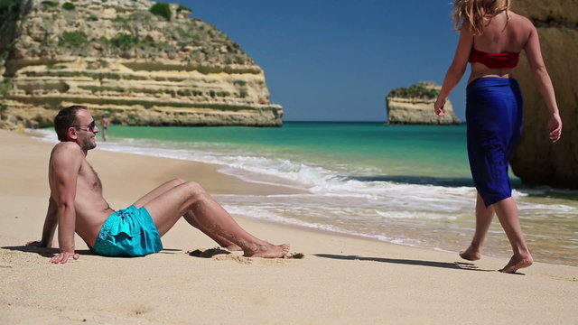 Man relaxing on beautiful beach, sexy woman walk by