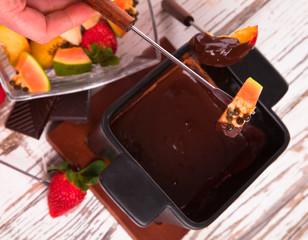Chocolate fondue with fresh fruits on wood