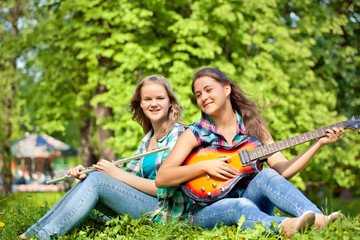 Fototapeta na wymiar two girls playing guitar and flute in the park