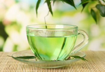 Transparent cup of green tea on bamboo mat, on nature
