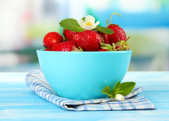 Ripe sweet strawberries in bowl on blue wooden table