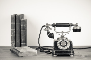 Vintage telephone, old books on table sepia photo