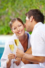 Mann küsst Frau mit Sekt am Pool